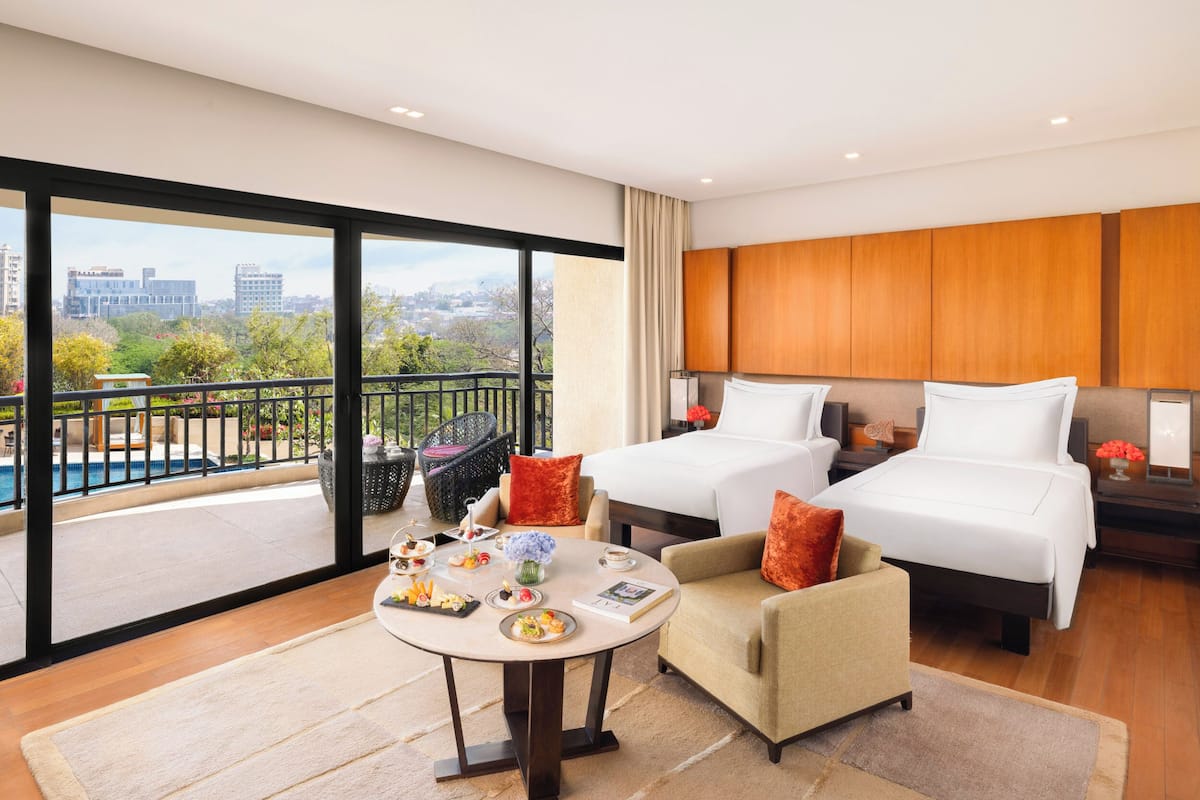 A hotel room with two beds, a balcony with a pool view, and a dining area with a table set for two.