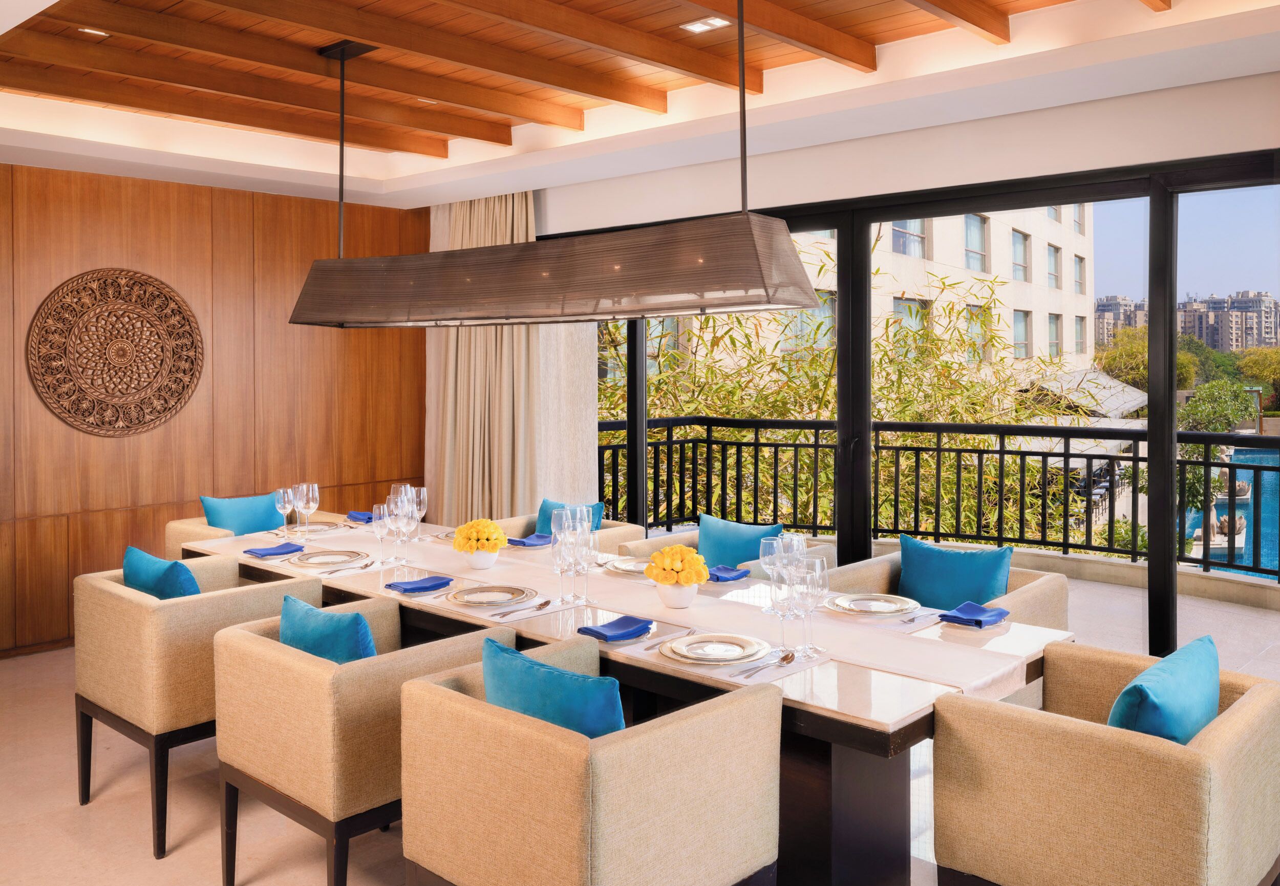 A dining area with a long table set for a meal, surrounded by chairs with blue cushions.