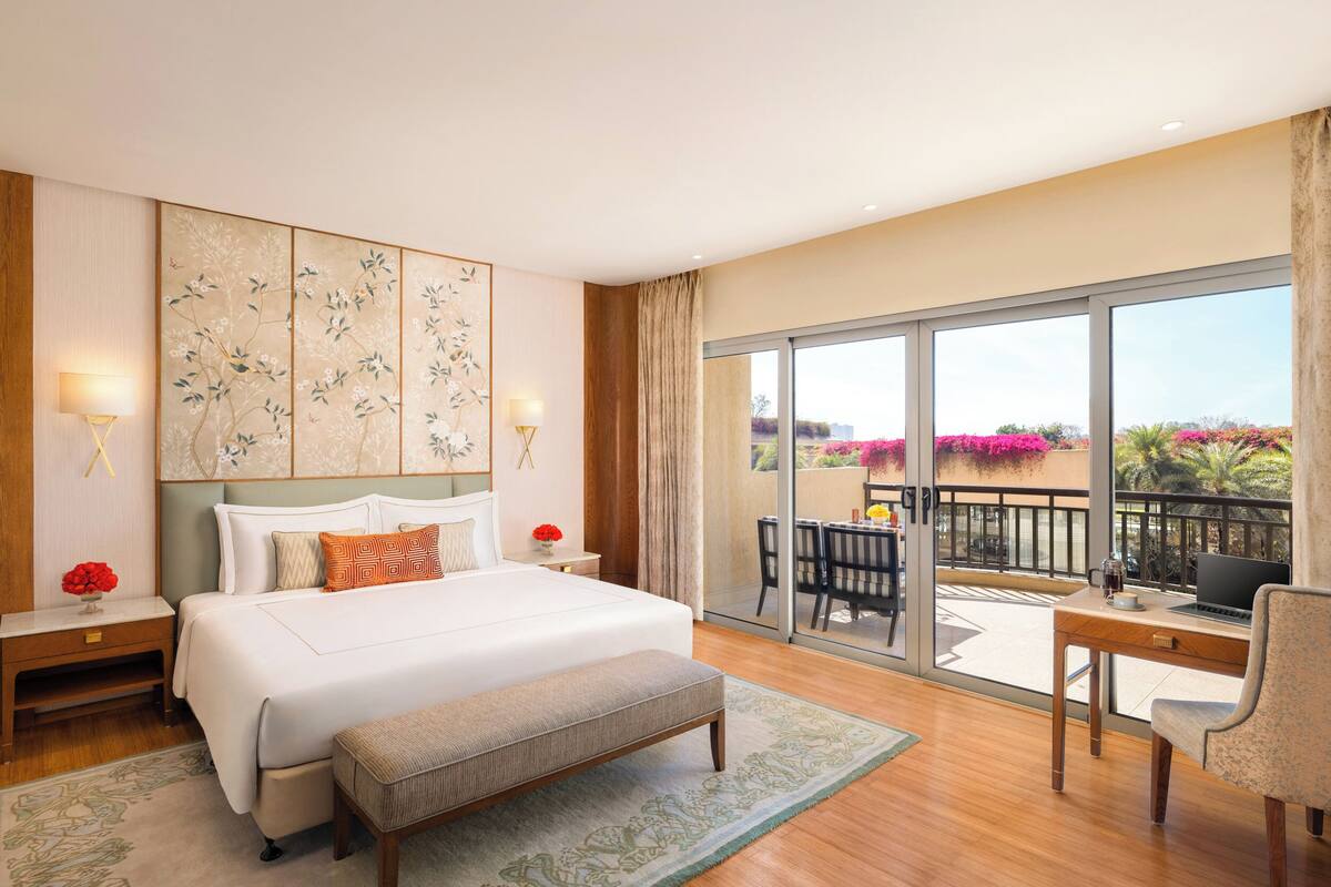 A hotel room with a large bed, a desk, a laptop, and a balcony with outdoor seating.