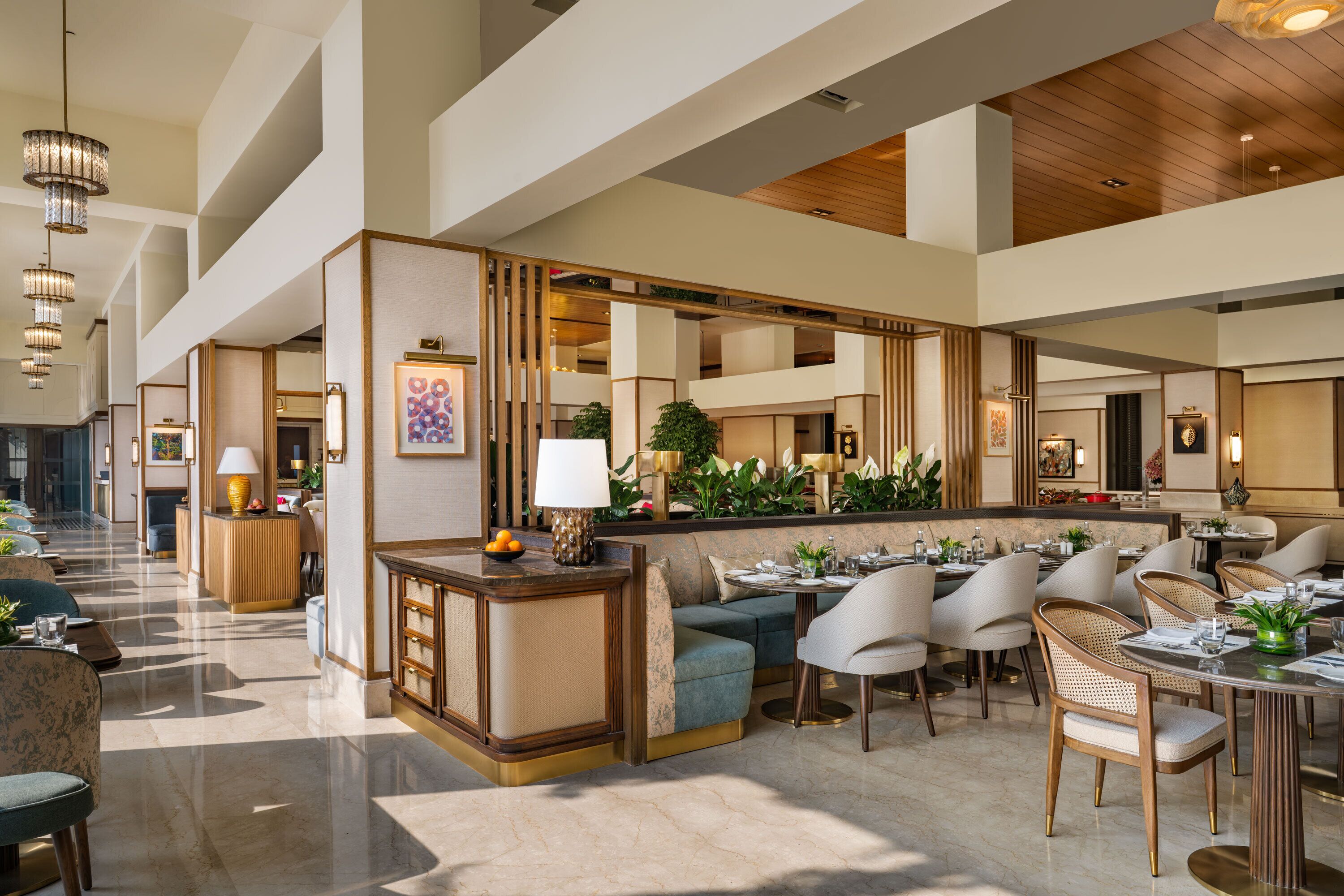 A spacious hotel lobby with a central seating area, multiple dining tables, and a reception desk.