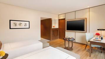 Una habitación de hotel moderna con un televisor de pantalla plana grande, un sofá, una mesa de comedor con sillas y una mesita auxiliar con flores.