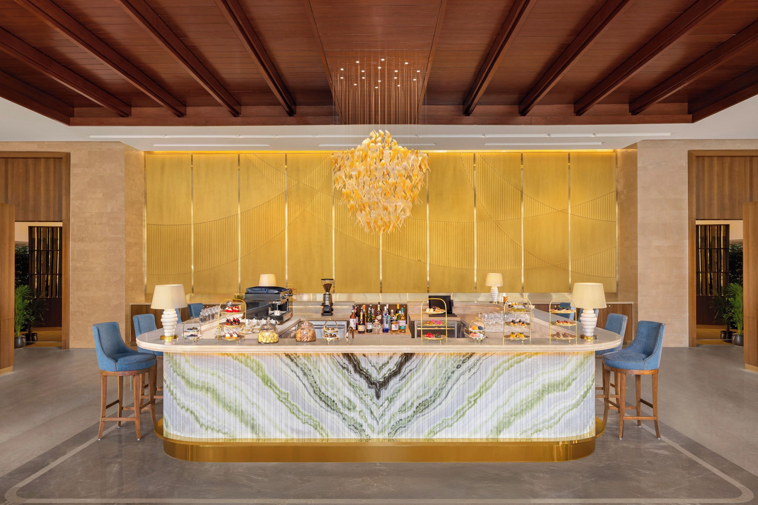 A modern bar area with a marble countertop, bar stools, and a decorative chandelier.