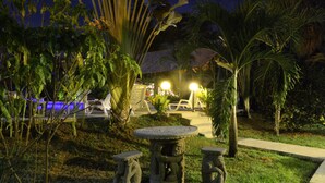 An outdoor garden area with stone tables and chairs, surrounded by lush greenery and palm trees. - La Villa Creole (Jacó)
