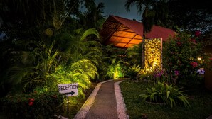 A reception area with a pathway leading to a building, surrounded by lush greenery and a stone wall. - La Villa Creole (Jacó)