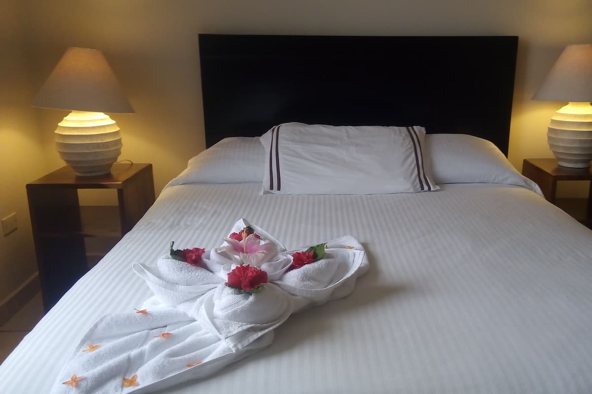 A neatly made bed with white linens and a towel arranged in a floral design on the bed.