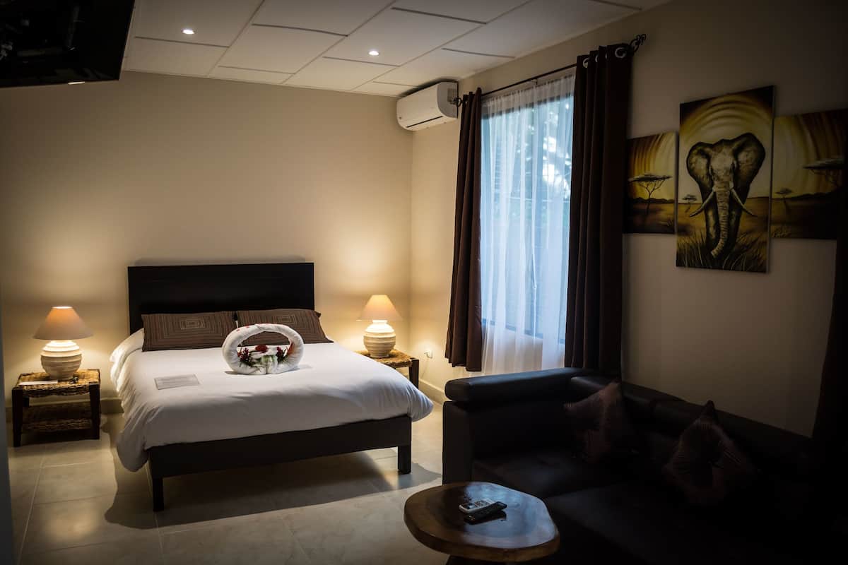A hotel room with a bed, a sofa, a round coffee table, and a painting on the wall.