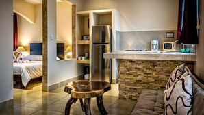 A compact hotel room with a kitchenette, a bed, a sofa, and a small wooden table. - La Villa Creole (Jacó)