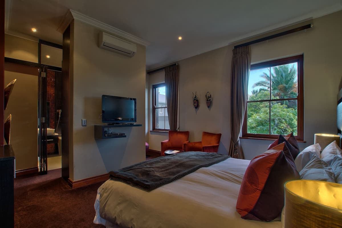 A hotel room with a bed, a TV, a desk, two chairs, and a window with a view of trees.