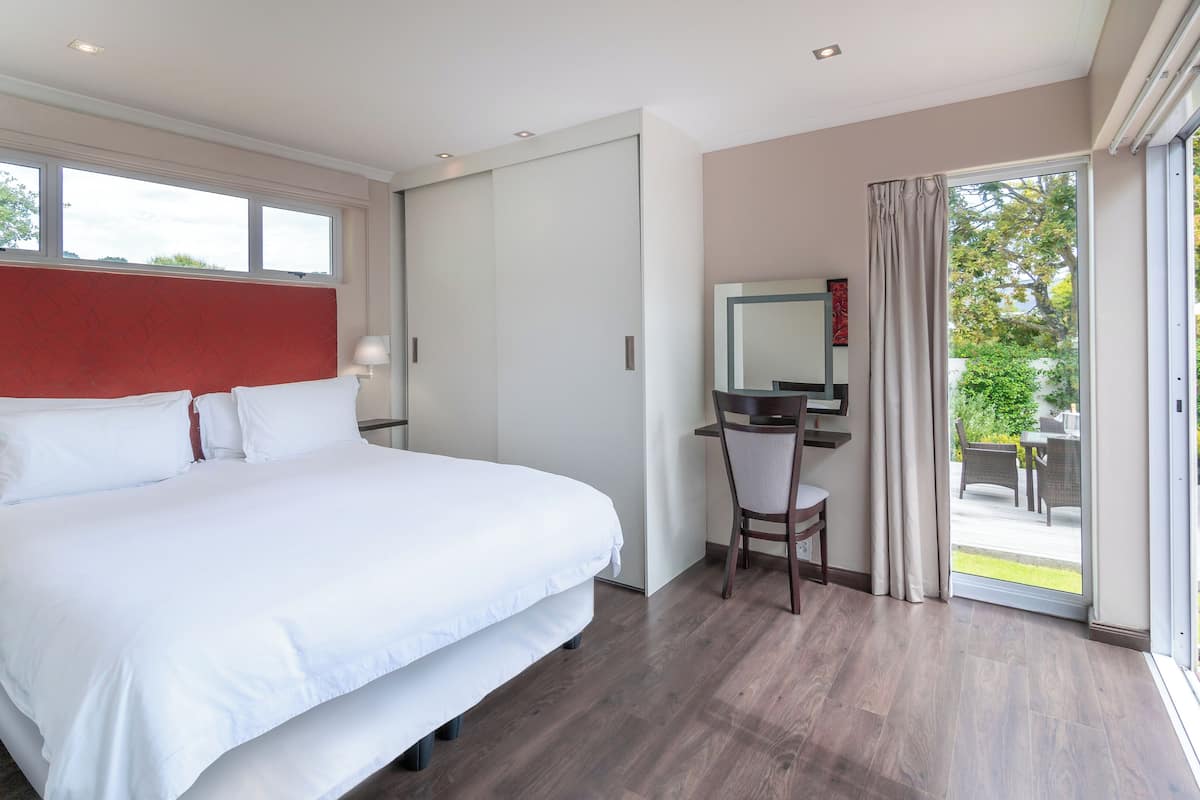 A modern hotel room with a large bed, a desk with a chair, and a sliding glass door to a balcony.