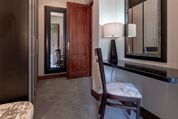 A hallway with a wooden door, a chair with a patterned cushion, a lamp, and a mirror on the wall. - Nova Constantia Boutique Residence (Cape Town)