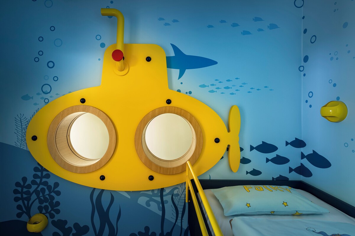 A child's bedroom with a submarine-themed wall mural, a bed with a pillow labeled 'Funky,' and a yellow toy submarine.
