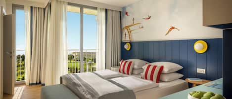 A hotel room with a bed, a desk with a bowl of apples, a view of greenery outside, and a mural on the wall.