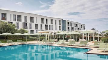 A swimming pool with lounge chairs and umbrellas, a white building with balconies, and a clear sky.
