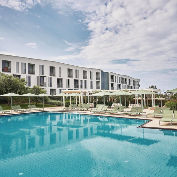 A swimming pool with lounge chairs and umbrellas, a white building with balconies, and a clear sky. - Falkensteiner Family Hotel Diadora (Zadar)