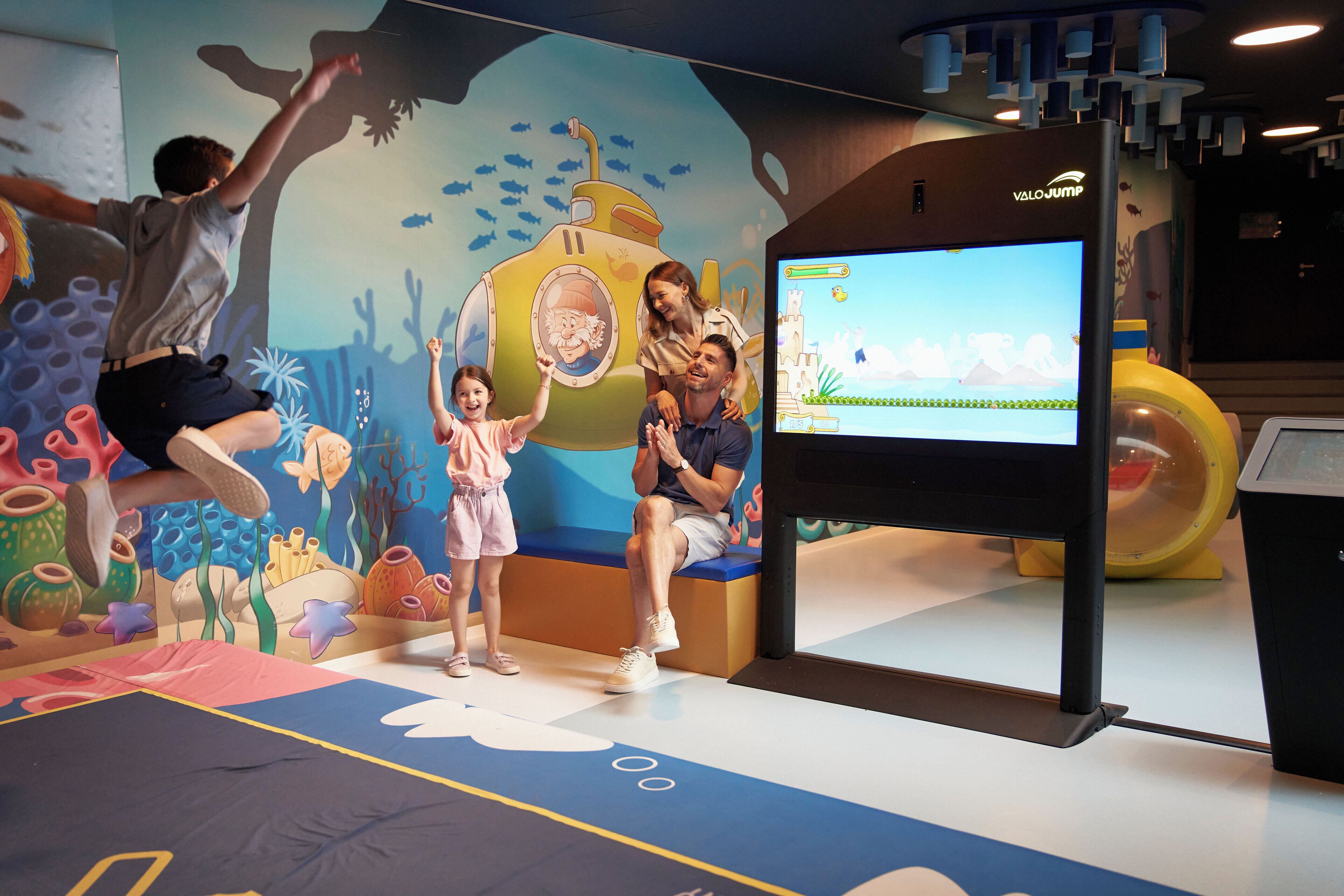 An indoor play area with a submarine-themed mural, a digital screen, and a play structure.