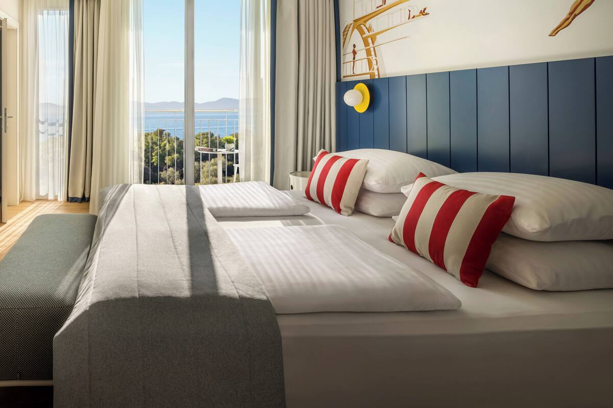 Ein Hotelzimmer mit einem großen Bett, Meerblick und einem Wandbild von Schwimmern.