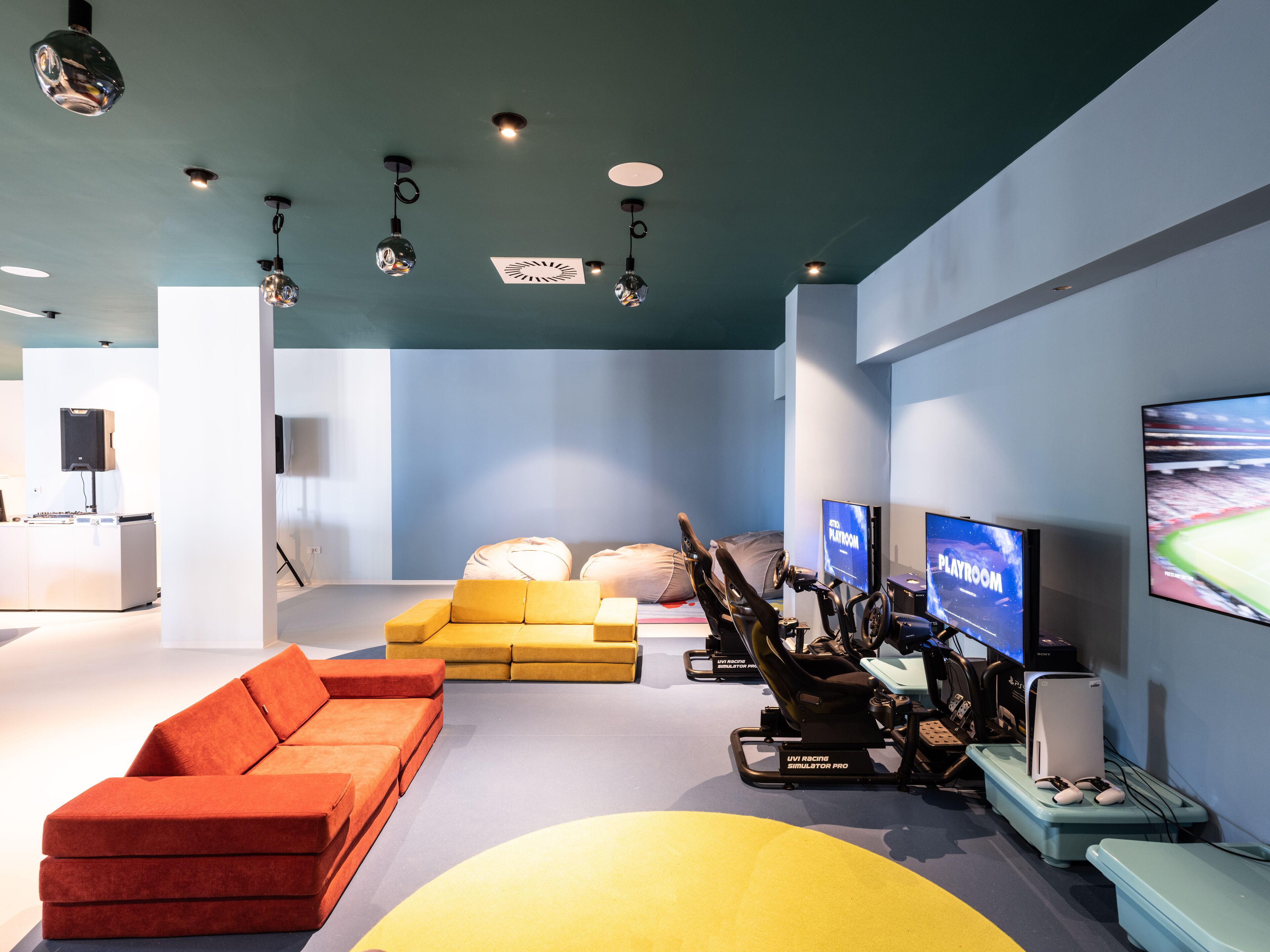 Ein modernes Wohnzimmer mit einem gelben Sofa, einem roten Couchen und einer Gaming-Einrichtung inklusive Rennsimulator und mehreren Bildschirmen.