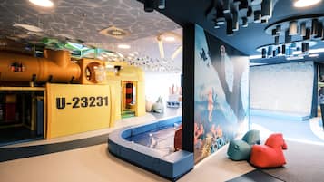 Children can play on the large play structure and relax in the padded seating area with a small pool nearby.