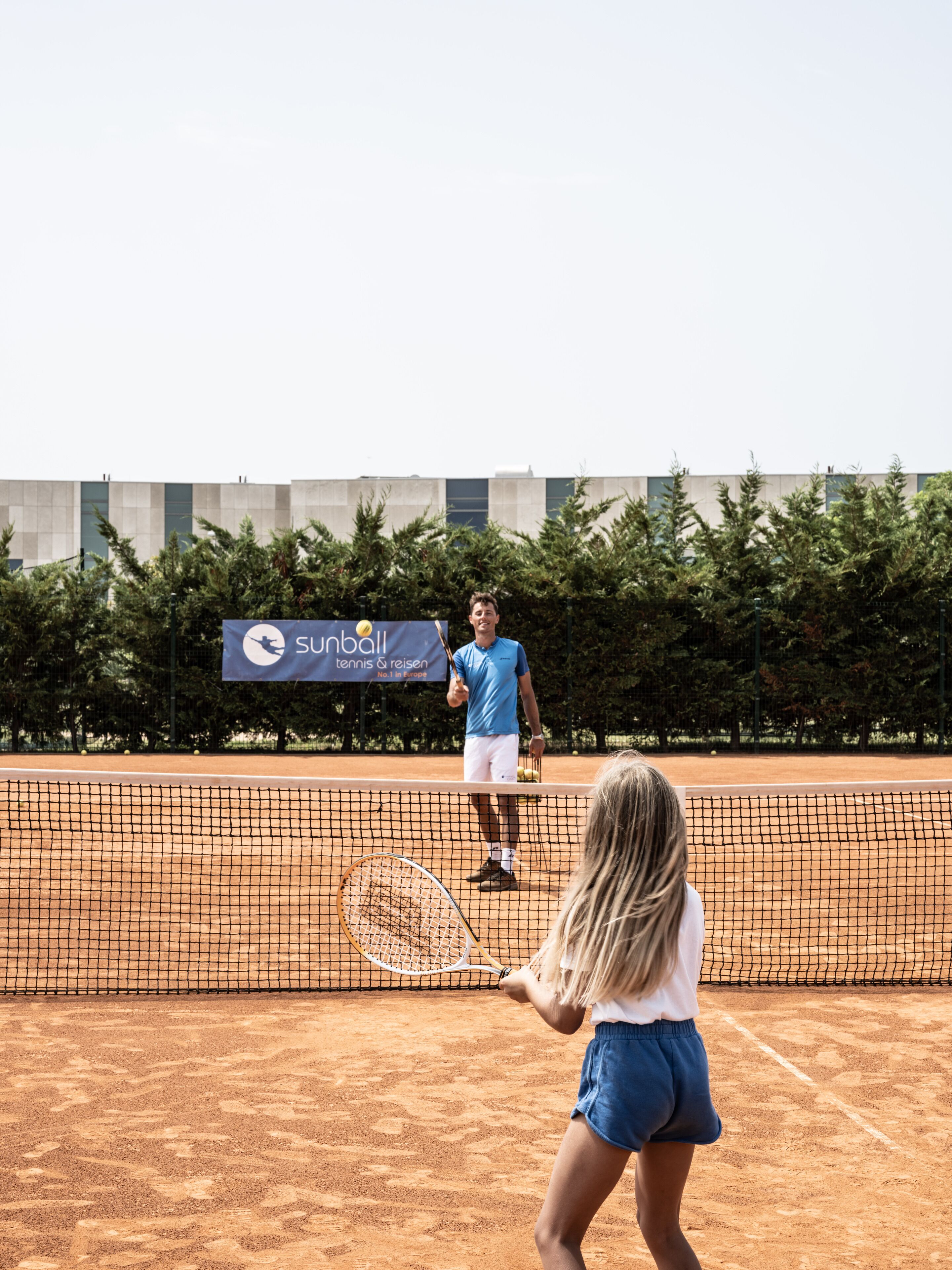 A tennis court with a net, a player in a blue shirt and white shorts, and a female player in a white shirt and blue shorts.