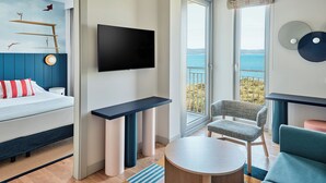 A modern hotel room with a bed, a TV, a desk, a chair, and a balcony with a view of the sea. - Falkensteiner Family Hotel Diadora (Zadar)