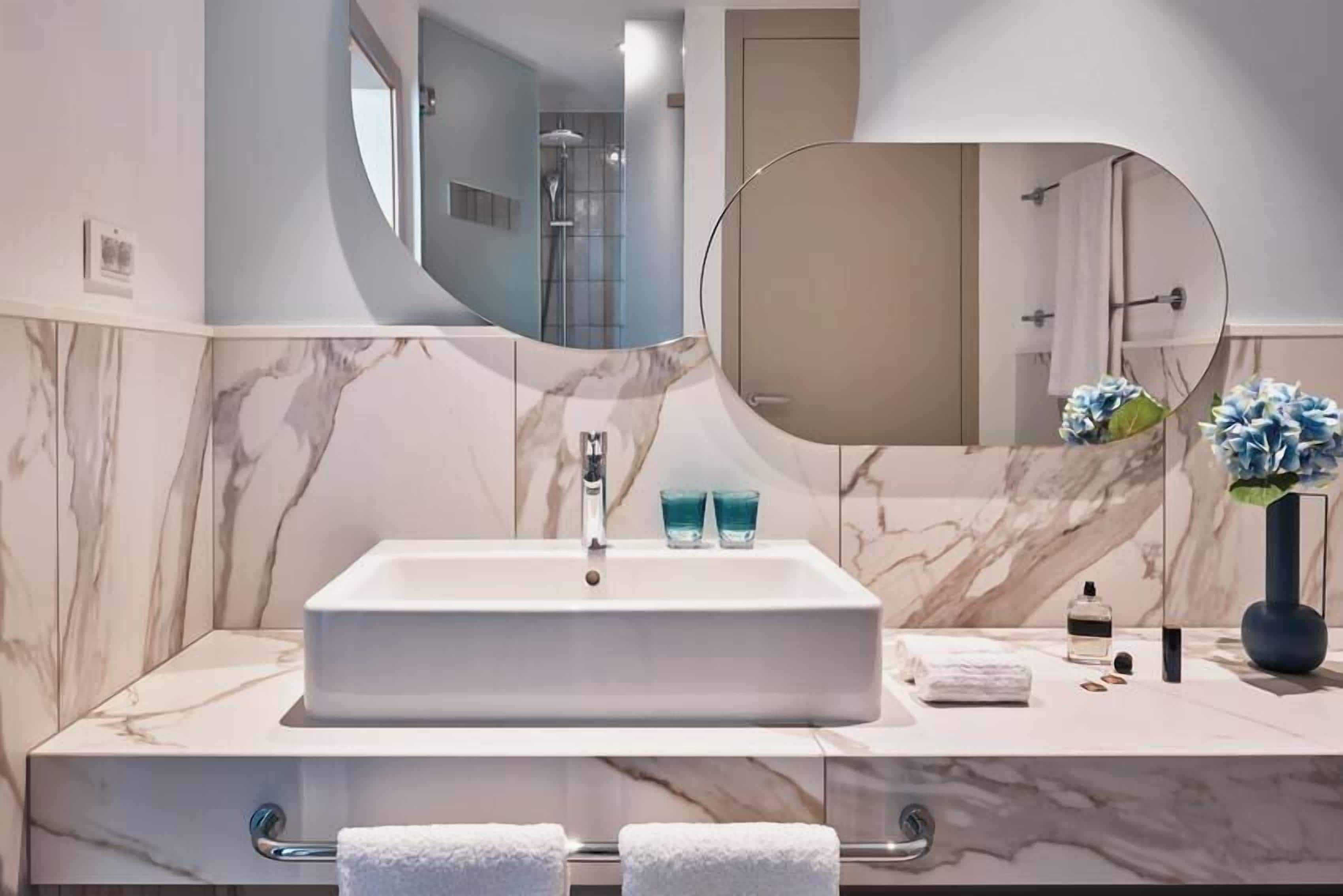 A bathroom with a marble sink, a large mirror, and a shower area.
