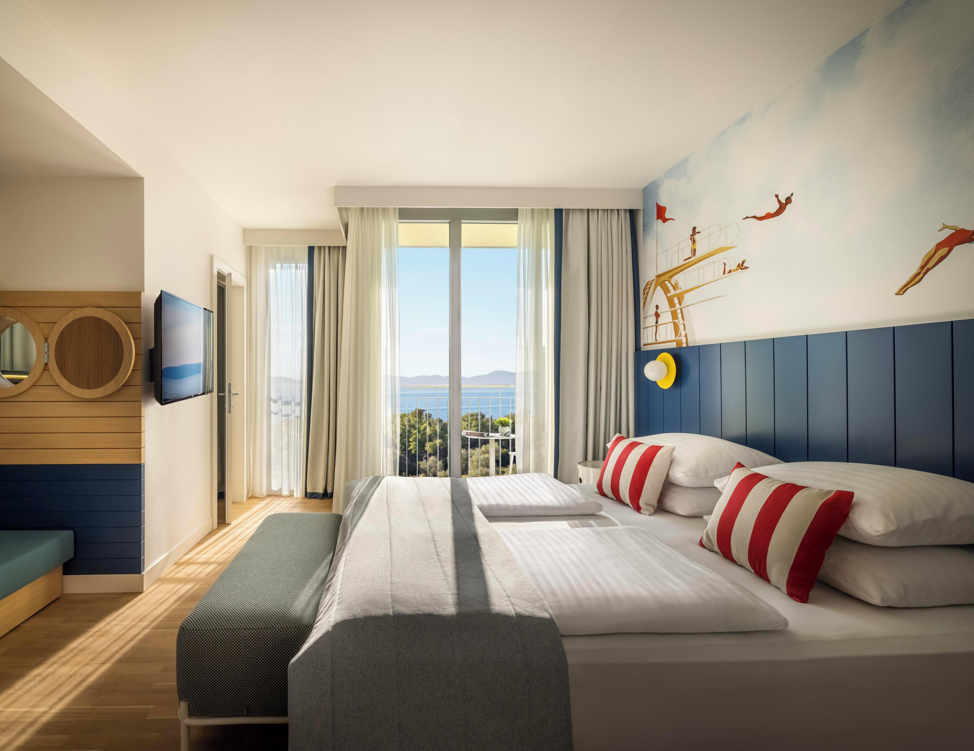 A hotel room with a large bed, a TV, a balcony with a view, and a wall mural.