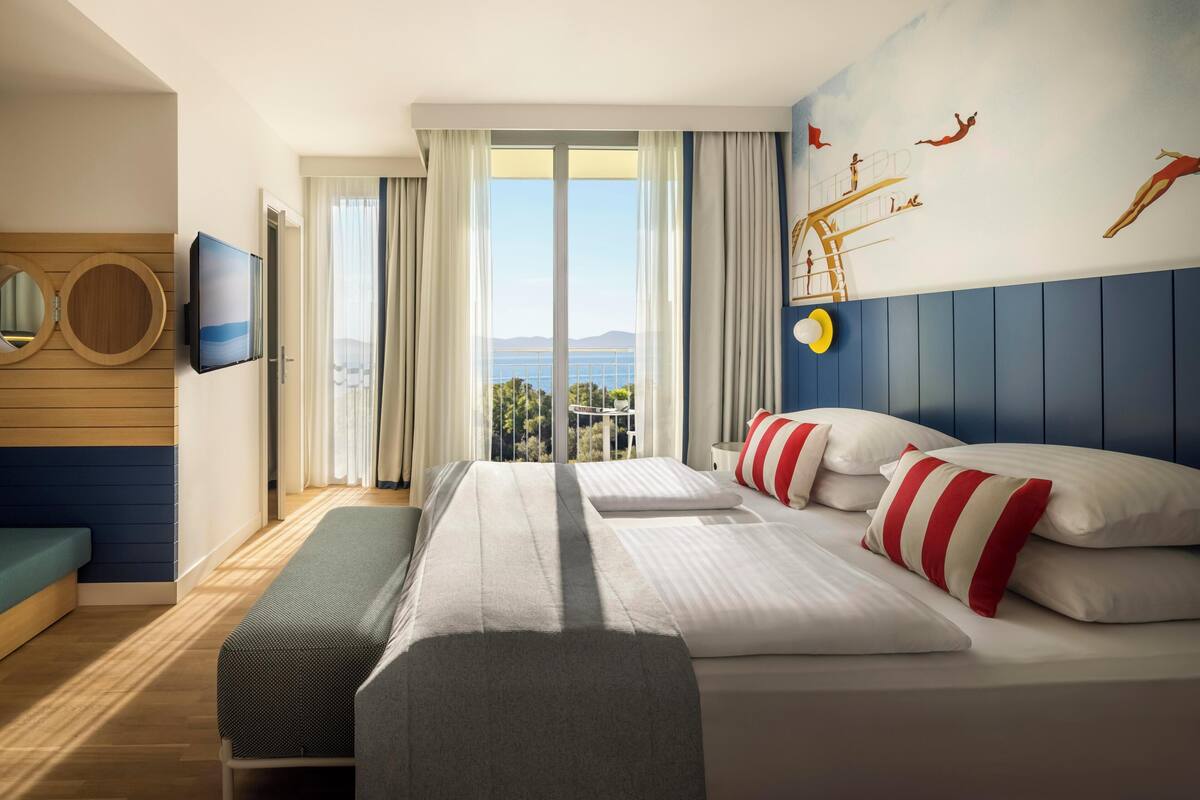 Ein Hotelzimmer mit einem großen Bett, einem Fernseher, einem Balkon mit Aussicht und einem Wandbild.