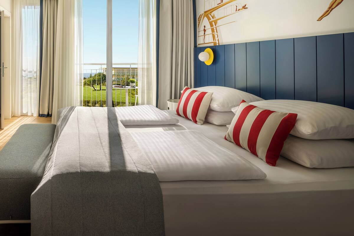 Ein Hotelzimmer mit einem großen Bett, Blick ins Freie und einem Wandgemälde.