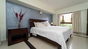 Un dormitorio con cama, una mesita de noche, un jarrón con flores y vistas al exterior a través de una ventana.
