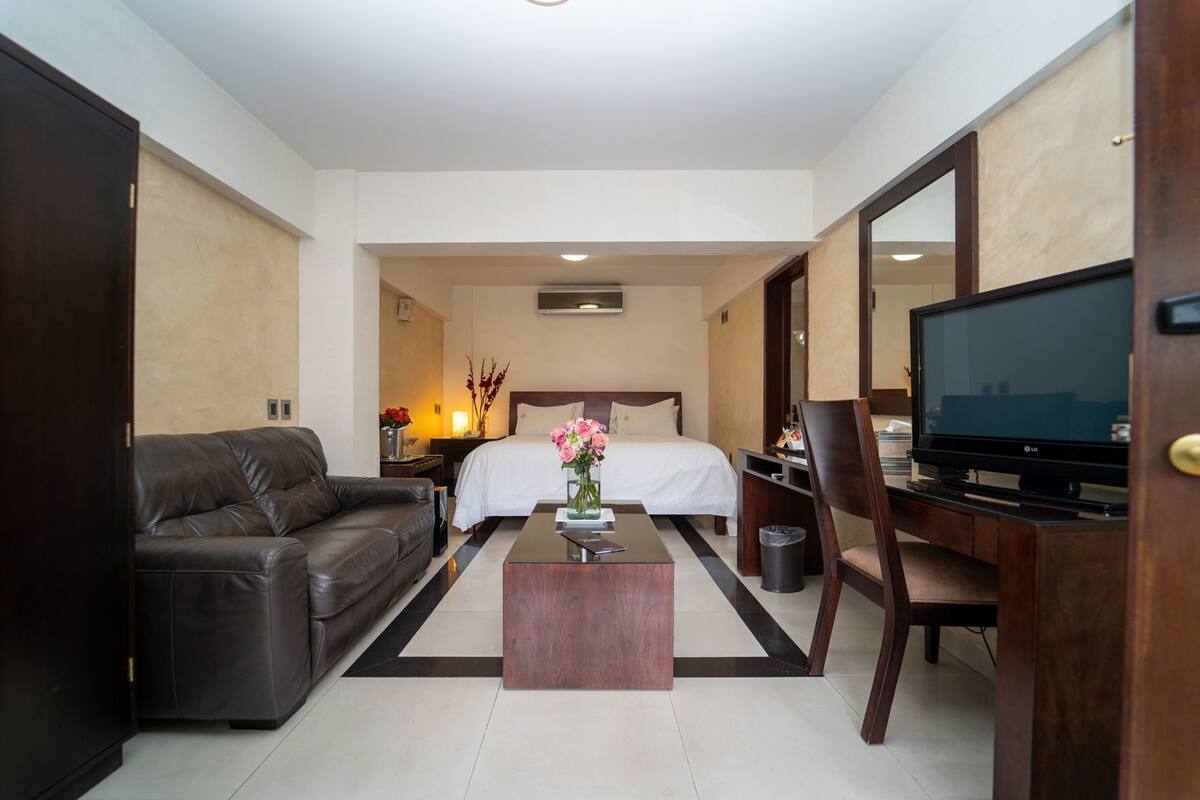 A hotel room with a bed, a leather sofa, a TV, and a coffee table.
