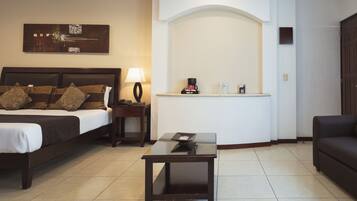 A hotel room with a bed, a small table, a lamp, a coffee maker, and a sofa.