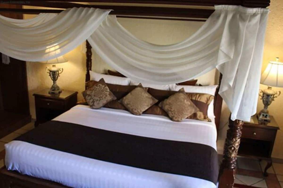 A four-poster bed with draped curtains, a wooden headboard, and multiple pillows.