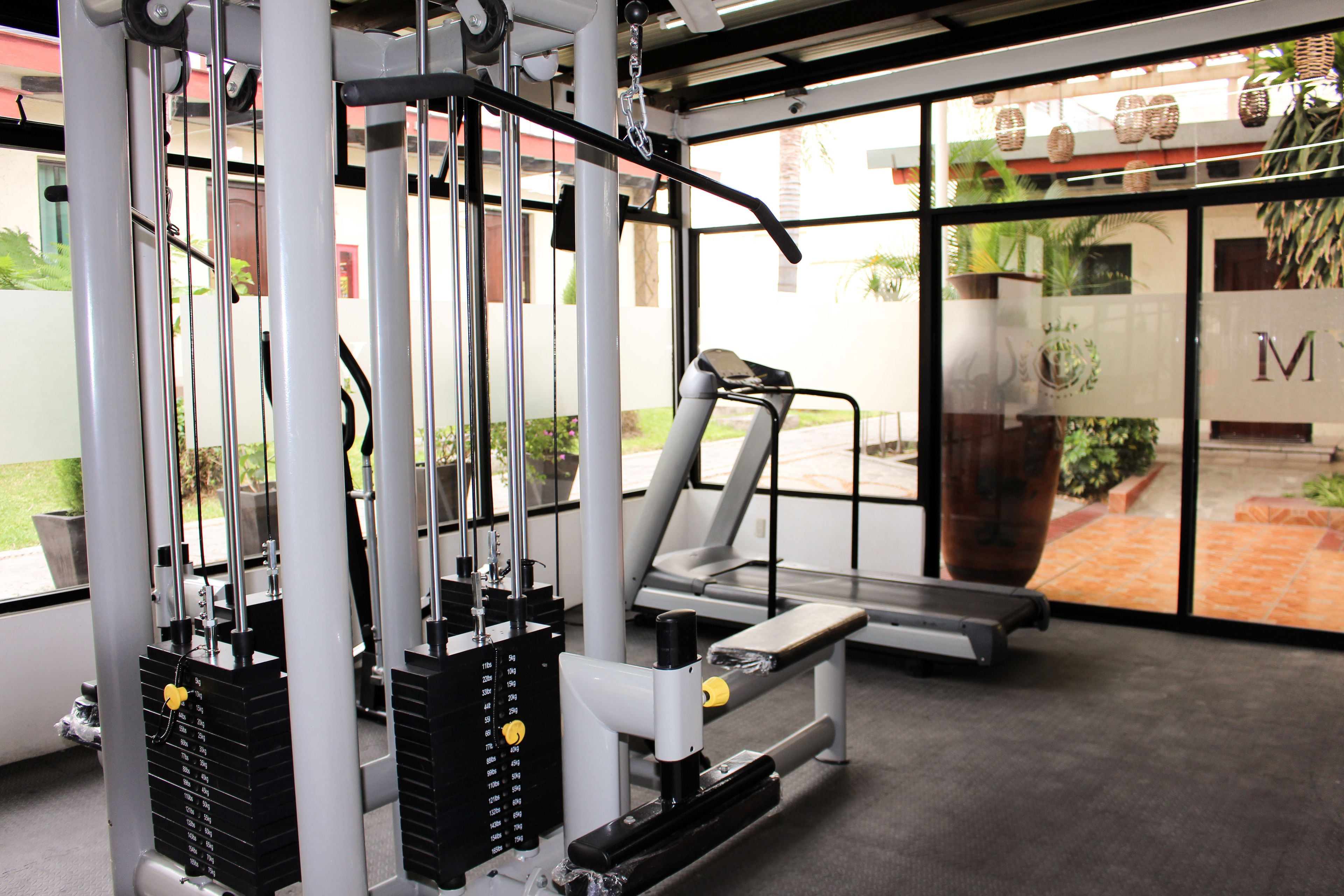 Une salle de sport équipée de matériel d’exercice, d’un tapis de course et de grandes fenêtres donnant sur l’extérieur.