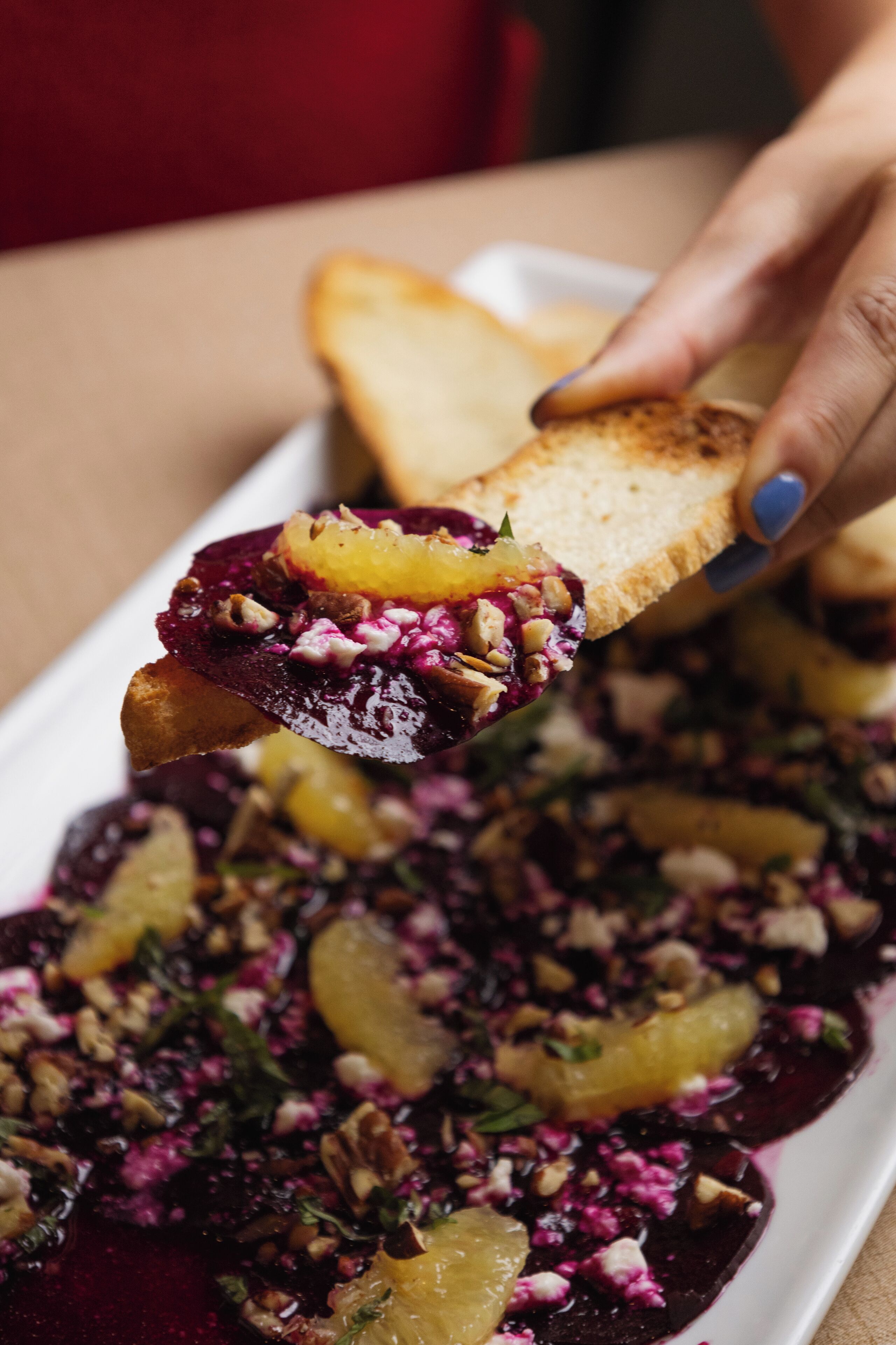 A close-up of a dish with beets, nuts, and possibly goat cheese, being served on a slice of bread.
