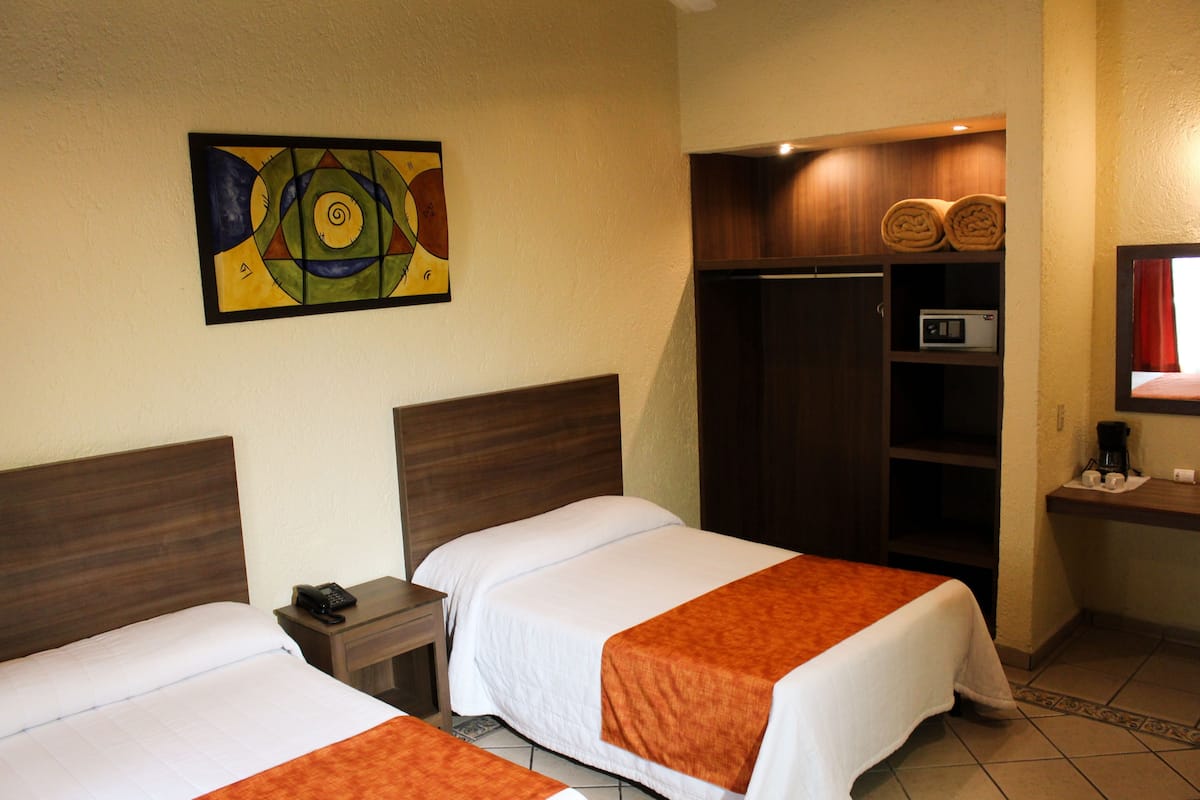 A hotel room with two beds, a painting on the wall, a wardrobe, a microwave, and a coffee maker.