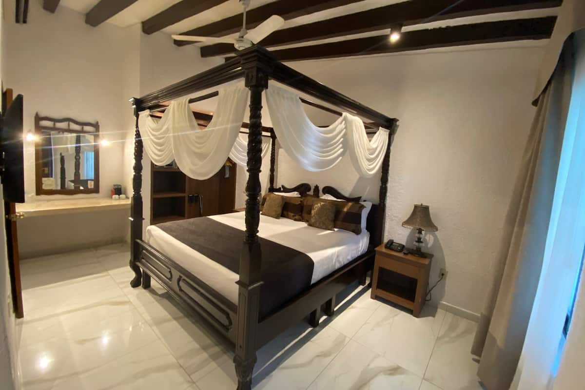 A four-poster bed with draped curtains, a bedside table with a lamp, and a mirror on the wall.