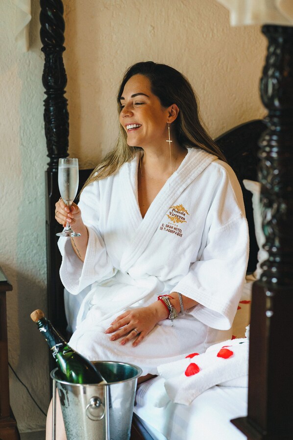 A person in a white robe holding a champagne glass, sitting next to a bucket with a bottle of champagne. - Hotel Posada Virreyes (Tlaquepaque)