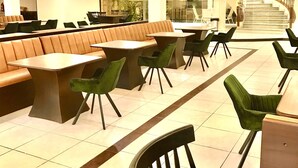 Un vaste espace de restauration intérieur doté de tables hautes et de banquettes, de ventilateurs de plafond et d’un escalier menant à un niveau supérieur.