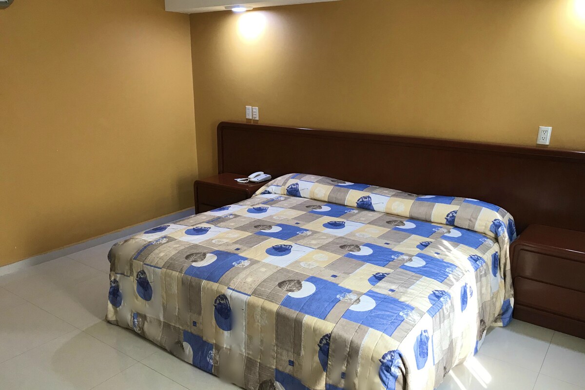 A hotel room with a bed, a nightstand, and a wall socket.