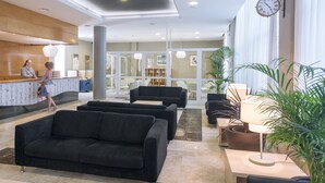 A modern lobby with a reception desk, black sofas, a coffee table, and potted plants. - Aparthotel CYE Holiday Centre (Salou)