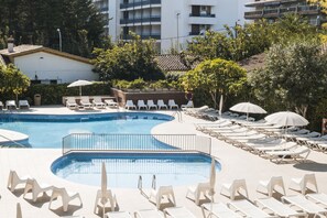 A pool area with lounge chairs and umbrellas, surrounded by greenery and buildings. - Aparthotel CYE Holiday Centre (Salou)