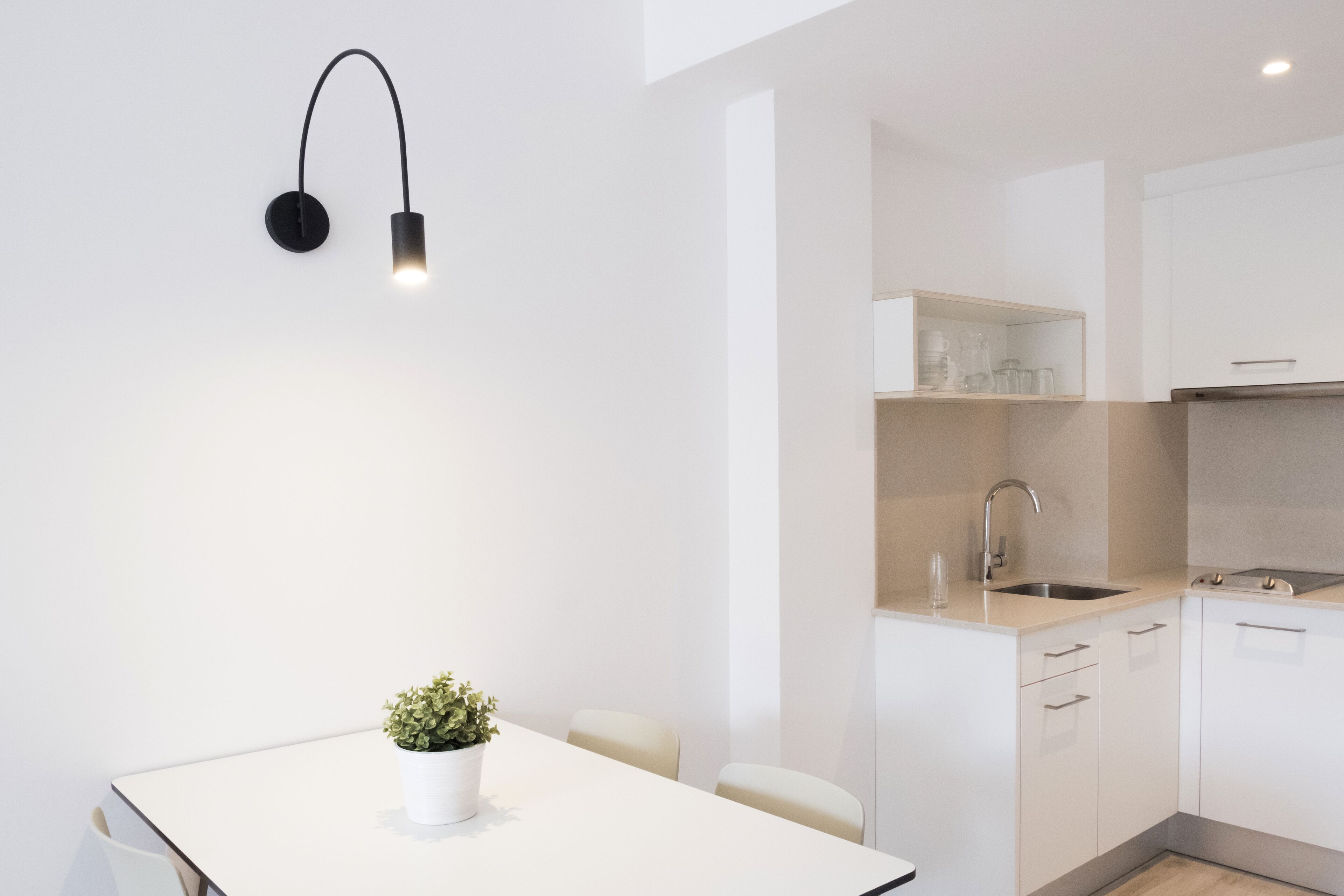 Una cocina moderna con armarios blancos, un lavamanos de acero inoxidable y una lámpara colgante negra.