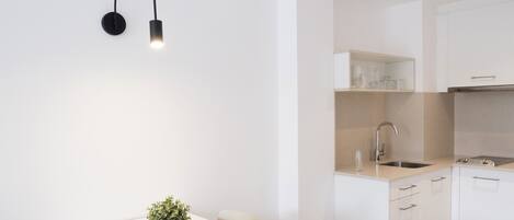 Una cocina moderna con armarios blancos, un lavamanos de acero inoxidable y una lámpara colgante negra.