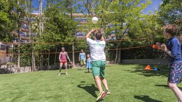 A person playing volleyball in a grassy area with trees and a building in the background.