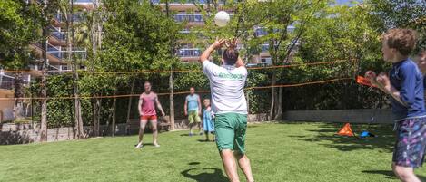 A person playing volleyball in a grassy area with trees and a building in the background.
