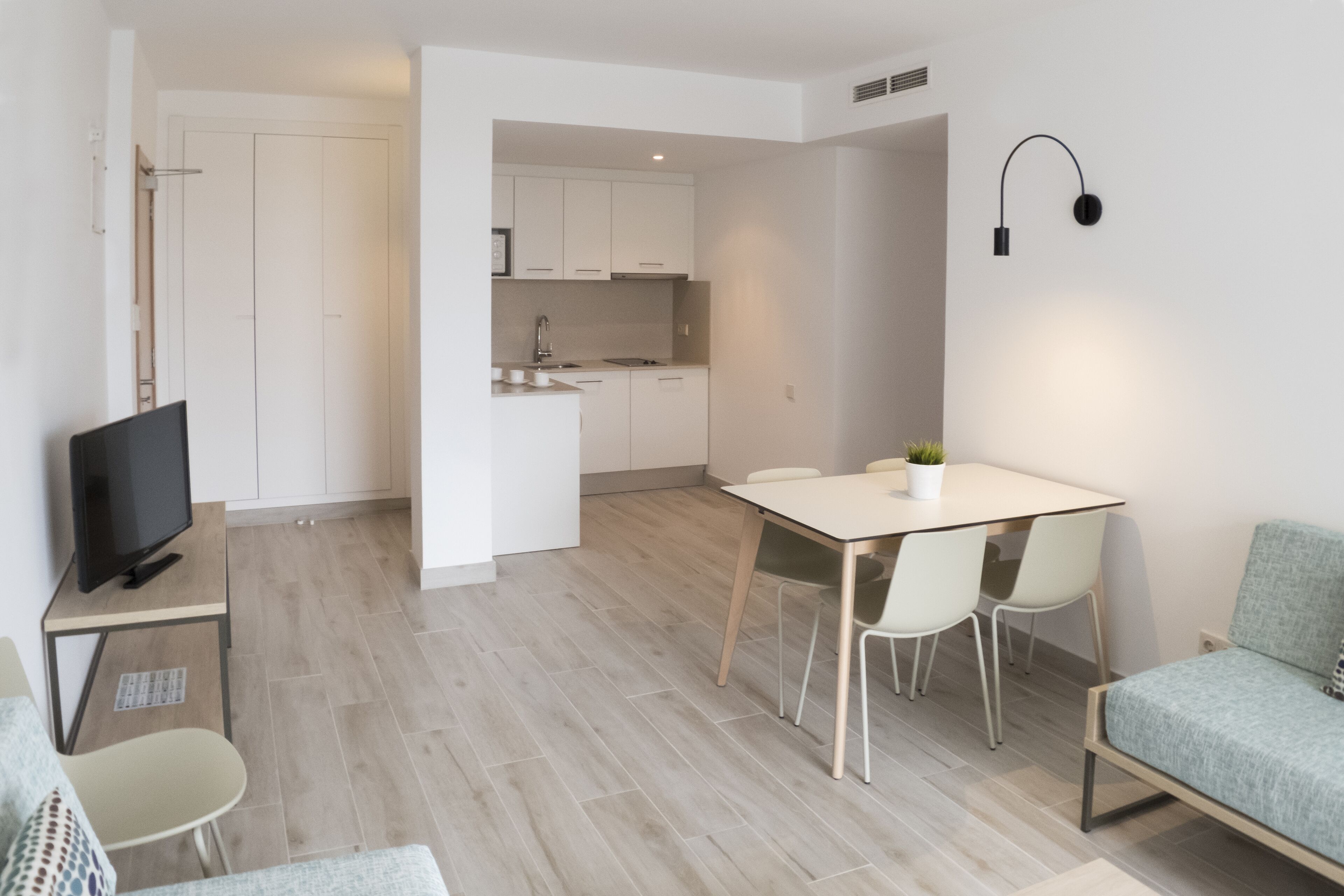 A modern living space with a dining area, a kitchenette, and a TV on a stand.