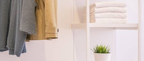 A white shelf with folded towels and a potted plant.