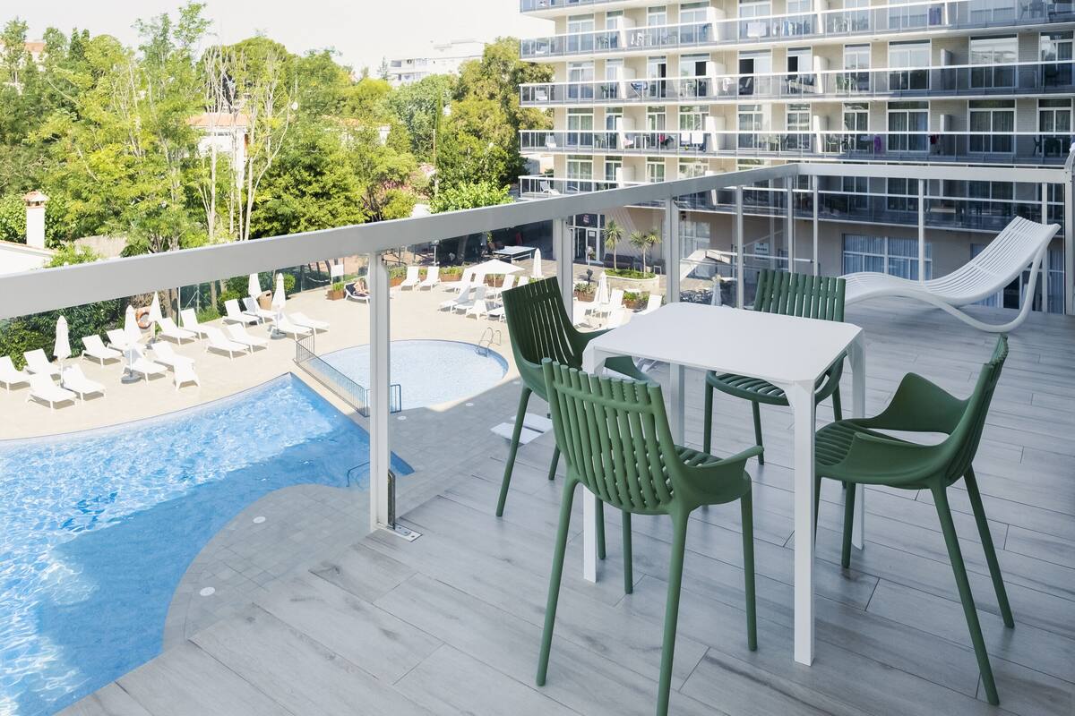 Área de piscina no terraço com mesa, cadeiras, piscina e vista para um edifício com varandas.
