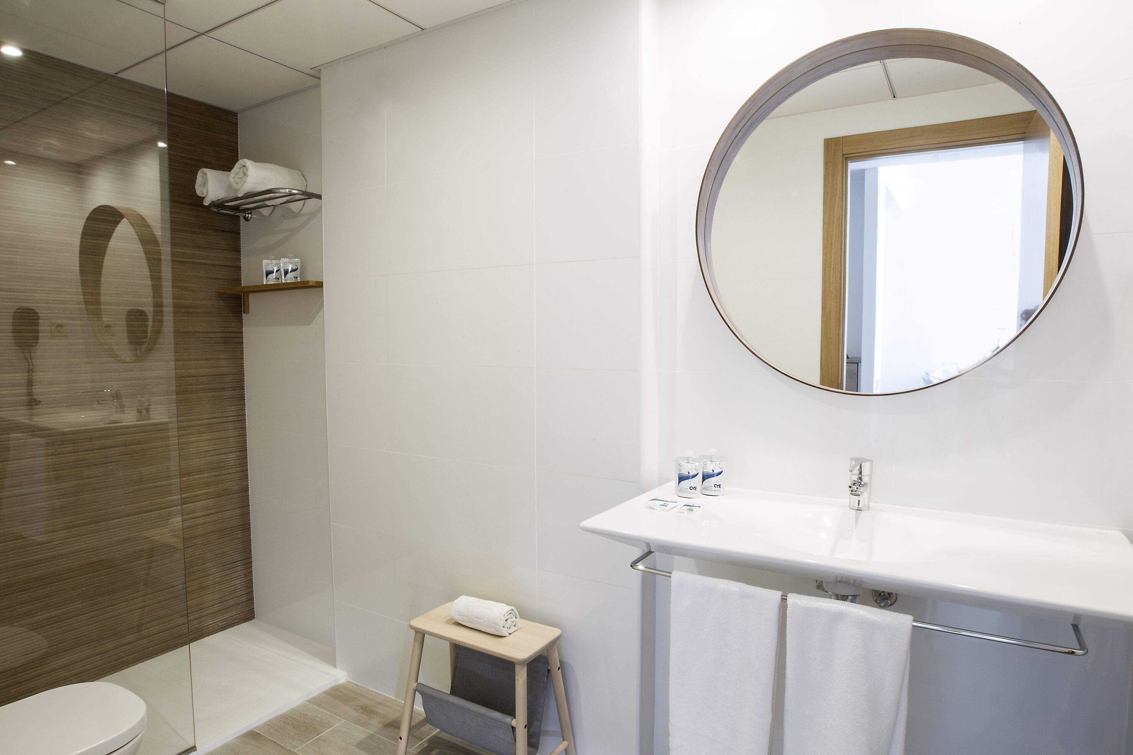 Une salle de bain moderne comprenant des toilettes, un espace douche, un lavabo avec un miroir et un petit marchepied.