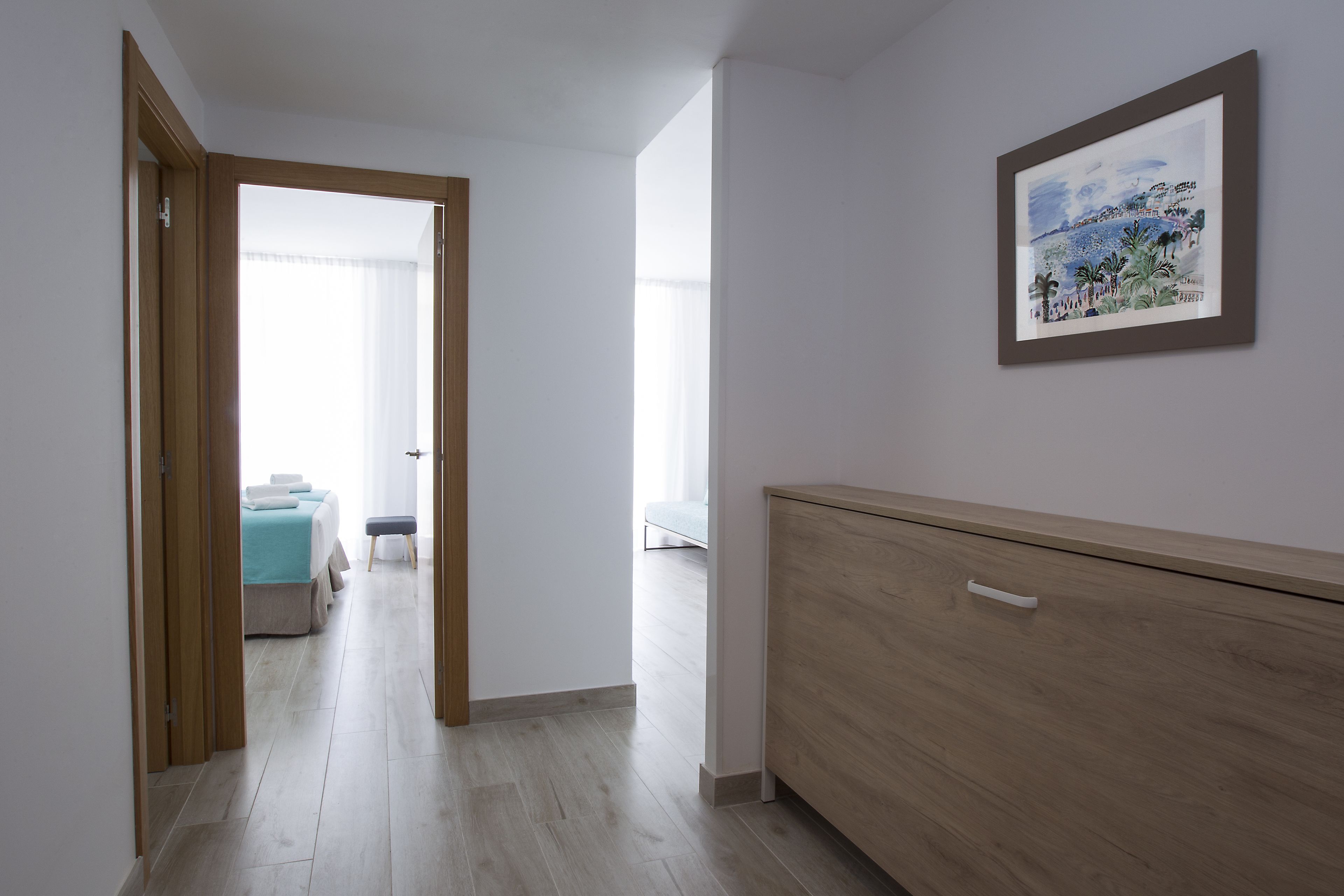 Hotellihuoneessa on puinen lipasto, valkoisilla vuodevaatteilla varustettu sänky, penkki ja seinällä taulu.